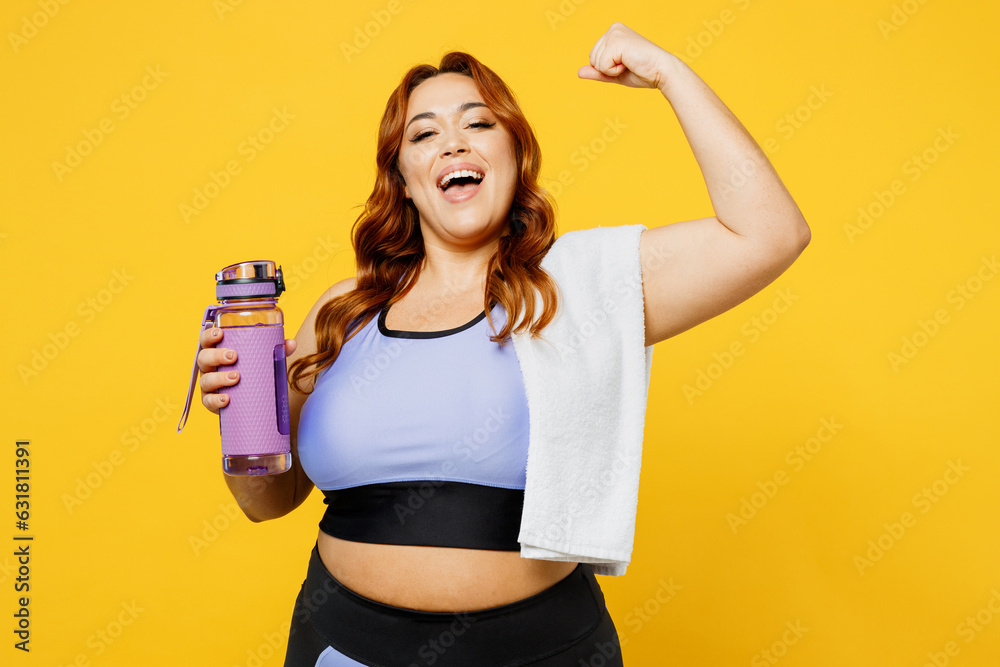 Young chubby overweight plus size big fat fit woman wear blue top warm up train hold towel bottle drink water do winner gesture isolated on plain yellow background studio gym. Workout sport concept. Young chubby overweight plus size big fat fit woman wear blue top warm up train hold towel bottle drink water do winner gesture isolated on plain yellow background studio gym. Workout sport concept.