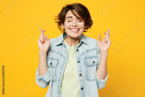 Fotografía Young worried woman wear green t-shirt denim shirt casual clothes waiting for special moment, keeping fingers crossed, making wish, eyes closed isolated on plain yellow background