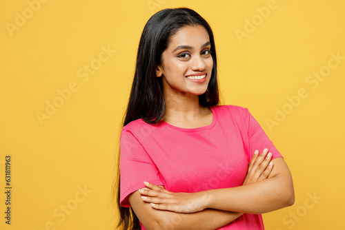 Side view young smiling happy cheerful Indian woman wearing pink t-shirt casual clothes holding hands crossed folded look camera isolated on plain yellow background studio portrait. Lifestyle concept.