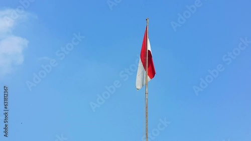 The Indonesian red and white flag fluttering by the wind with blue sky and clouds in background