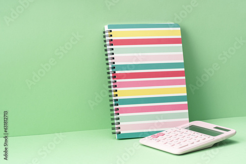 One stripy pastel spiralbound notepad and calculator on green. Back to School or drawing and creativity concept. Copy space. Mockup photo