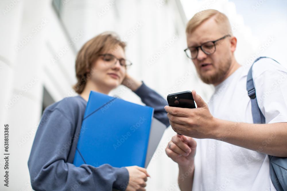 Obraz premium A man and a woman look at the screen of the smartphone and discuss something, laugh, phone close-up, students, young IT specialists