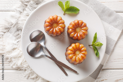 Canele is a small French pastry flavored with rum and vanilla with a soft and tender custard center and a dark, thick caramelized crust close-up in a plate on the table. Horizontal top view from above photo