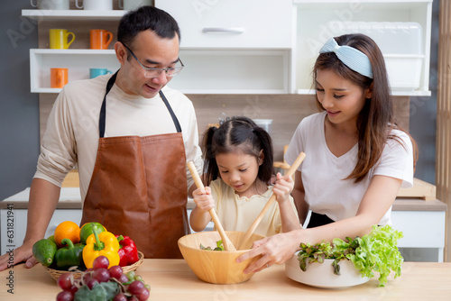 Happiness asian family with father, mother and daughter preparing cooking salad vegetable food together in kitchen at home, happy dad, mom and kid cooking breakfast with salad, lifestyles concept.