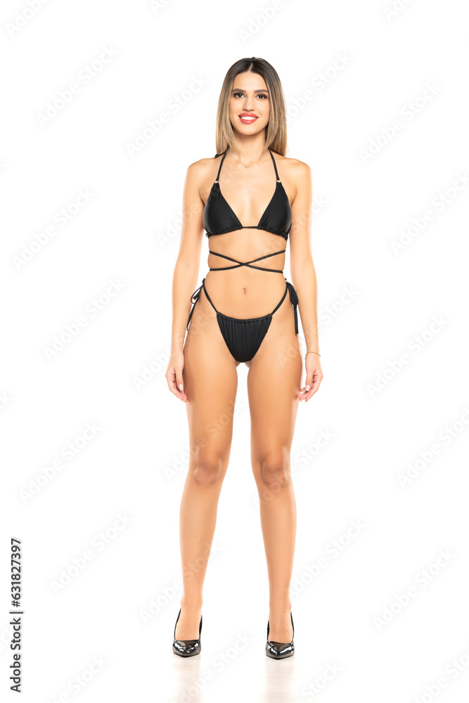 Pretty young smiling woman posing in black swimsuit on white background. Front view.