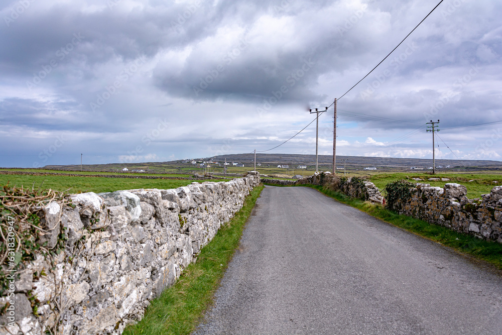 Scenic road with stone walls alongside on a bright sunny day with a clouds and blue sky on Inishmore island, Galway