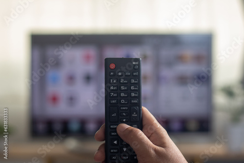 The man is watching TV and using a remote control to search for a program on the internet.