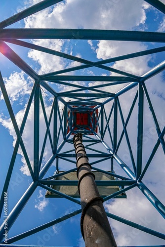 Vertical shot of an electrical power line tower structure with a cloudy blue sky in the background