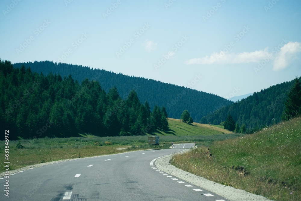Fototapeta premium Beautiful view of an asphalt road through green hills under a blue sky.