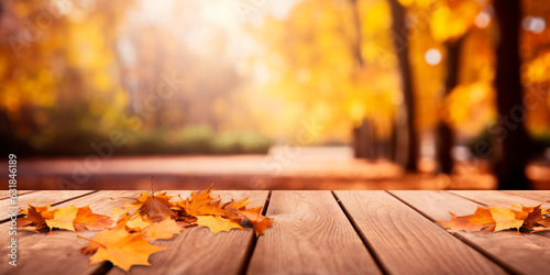 Wooden empty table with autumn yellow/orange leaves in front of blurred autumn park background.