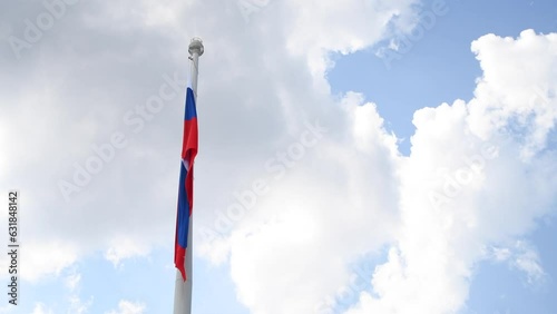 Low angle view of Russian national flag hanging on large flagpole against blue sky with white clouds in sunny summer windless day. Real time handheld video. Copy space. Politic symbols theme.