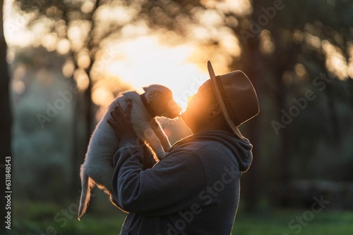 Caucasian man wearing a hat standing in a lush forest, while holding cute Golden Retriever at sunset
