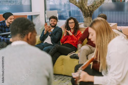 Young people applauding their female colleague while she is playing guitar and singing for them photo