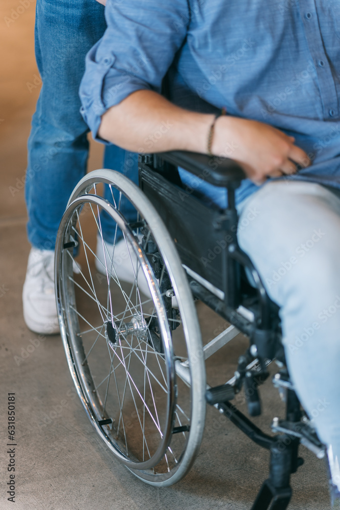 Disabled male employee in wheelchair pushed by his colleague. Colleagues helping each other Disabled male employee in wheelchair pushed by his colleague. Colleagues helping each other