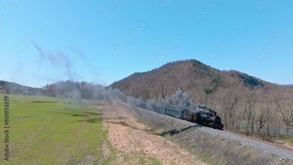 Slow-motion of a steaming train passing between leafless trees and fields during the daytime