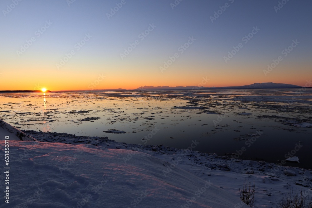 an area covered in snow and surrounded by water at sunset