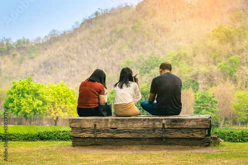 Back view of Asian family relaxing near mountain. Relax lifestyle for people enjoying freedom in summer holidays. Happy family outdoors resting together. Enjoying nature outdoors with mountain view. © JinnaritT