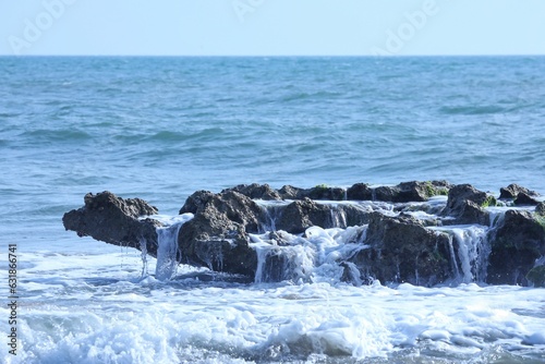 Scenic ocean view featuring a powerful wave crashing against large rocks on a sunny day
