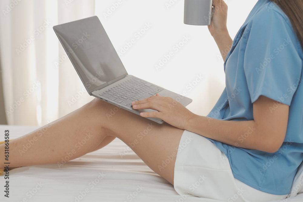 Naklejka premium Young Asian woman with beautiful face, long hair, blue shirt lying on bed in white bedroom at home with cup of coffee and video call with laptop talking to relatives on vacation. holiday concept.