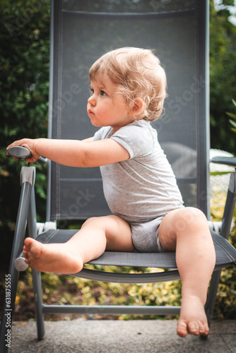 Baby auf Gartenstuhl schaut zur Seite und hält sich an Armlehne fest