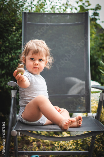 Baby auf Gartenstuhl zeigt Spielfigur in Kamera
