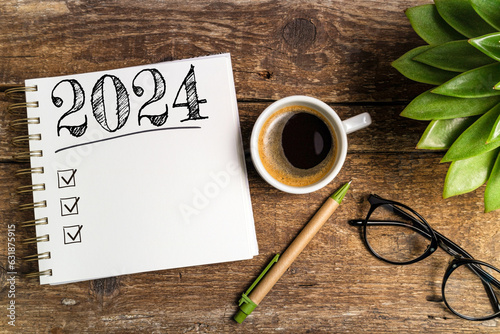 New year goals 2024 on desk. 2024 goals list with notebook, coffee cup, plant on wooden table. Resolutions, plan, goals, action, checklist, idea concept. New Year 2024 template, copy space