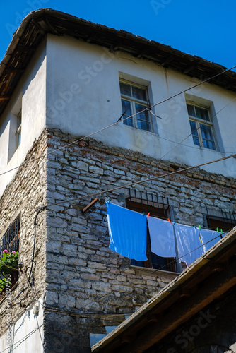Traditional stone house in Gjirokaster, Albania, with blue laundry hanging to dry against a vivid blue sky in warm summer sunlight.