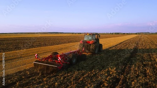 Aerial view of a Contemporary Red Combine tractor plowing and tilling field during sunset. City outskirts farming fimed from a bird's eye view. Tracking shot. 
 photo