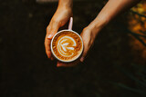 Young woman holding a cappuccino in her hands on a dark background. A stylish concept for advertising coffee. Delicious aromatic cappuccino with alternative milk