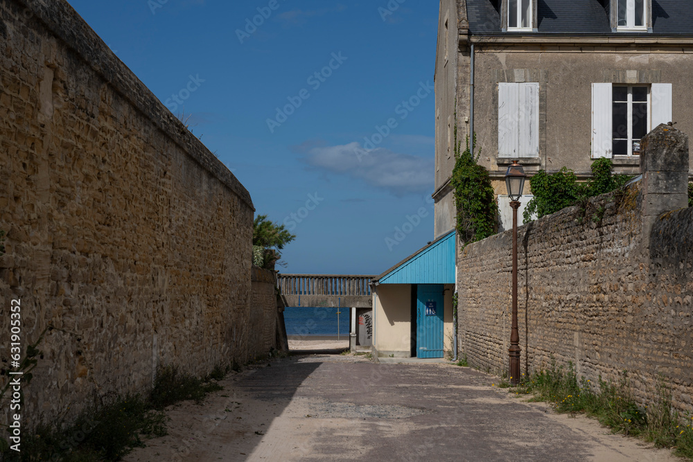 Saint-Aubin-Sur-Mer, France - 07 19 2023: View of a narrow passageway with stone houses joining the jetty and the beach.