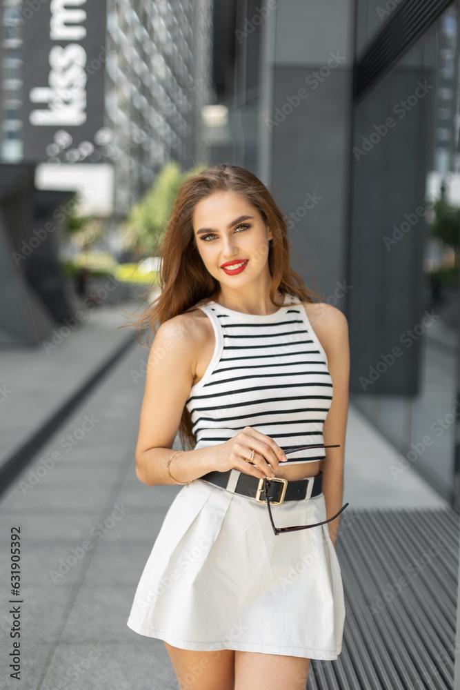 Happiness pretty fashion woman with smile with red lips in casual fashionable outfit with top and skirt walks in the city