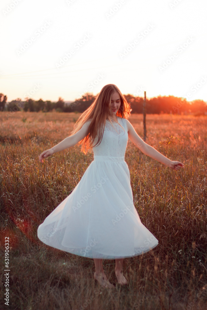 A beautiful pretty girl is dancing on a field at sunset in a white dress. Happy woman. Concept. Bride