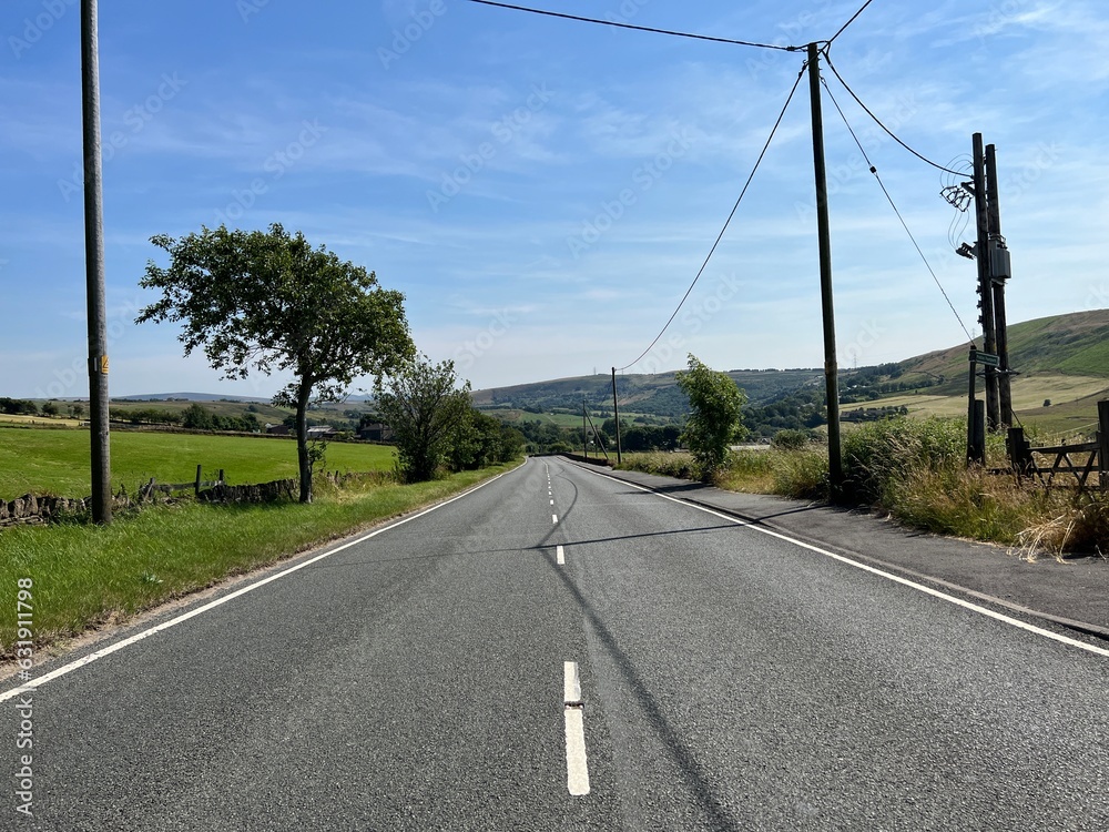 Late afternoon on, Ripponden Road, with stone walls, fields, and distant hills on a hazy day near, Oldham, UK