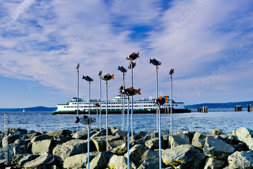 Public salmon sculpture with ferry in the background on a cloudy day
