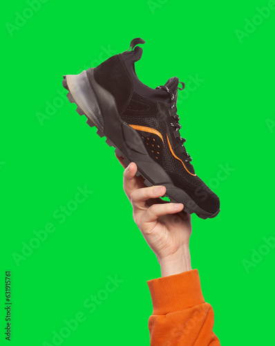 Man's hand holding modern black sneaker, isolated on a vibrant green background. Outlet marketing. Poster for selling sports footwear