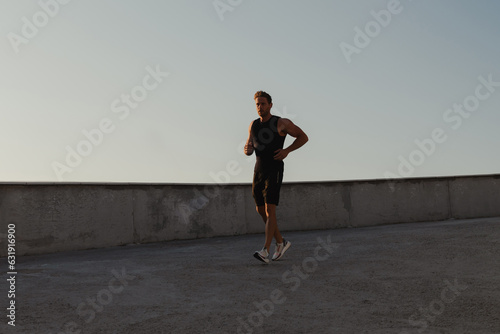 Athletic young man in sports clothing running by the road while enjoying morning jog outdoors