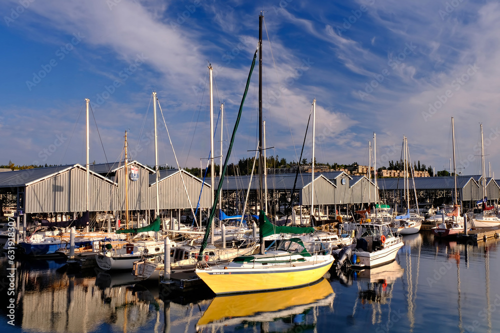 Fototapeta premium Yellow sailboat reflected in the water at sunset in a marina, with a blue sky and clouds in the background