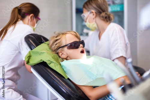 Lifestyle photo of little girl 5-6 year old visit dentist doctor, sitting in medical chair with open mouth. Kid girl treating teeth at dental office. Medical children dentistry concept. Copy ad space