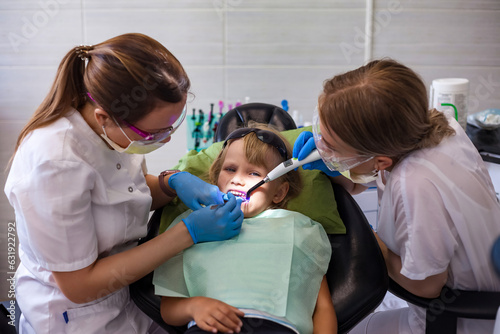 Dentist doctor and assistant doing teeth little girl 5-6 year old at dental office in clinic. Dentist having treating teeth treats kid girl. Concept of medical children dentistry. Copy ad text space