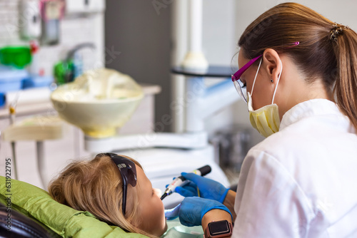 Realistic photo of dentist doctor having treating teeth little girl 5-6 year old at dental office. Dentist doing treats teeth kid girl in clinic. Concept of medic children dentistry. Copy text space