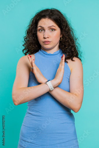 Young woman say No hold palm folded crossed hands in stop gesture, warning of finish, prohibited access, declining communication, body language, danger. Girl on blue background. Lifestyles. Vertical