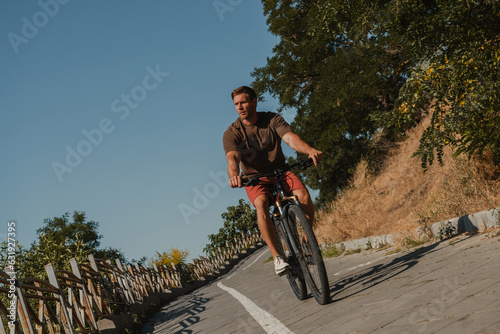 Confident young man riding bicycle by the scenic road outdoors