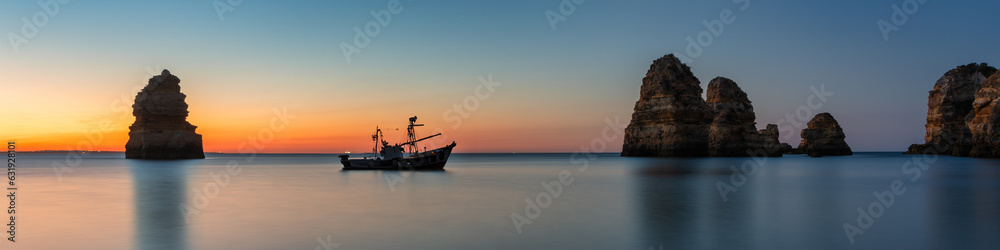 Coastal dream - Fishing boat anchors between two beautiful rocks at sunrise in Algarve Portugal
