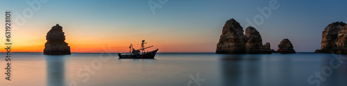 Coastal dream - Fishing boat anchors between two beautiful rocks at sunrise in Algarve Portugal © emotionpicture