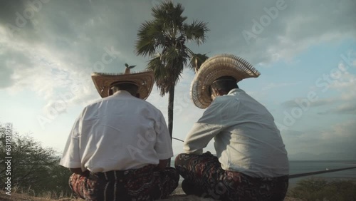 Two people sitting under the palm tree, playing string instrument of sasando in the afternoon photo