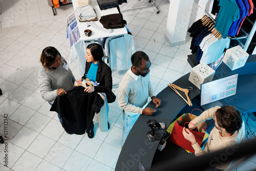 Shopping center cashier packing apparel and accepting payment while customers waiting at checkout desk top view. Diverse people buying clothes in boutique and standing in line at cash register photo