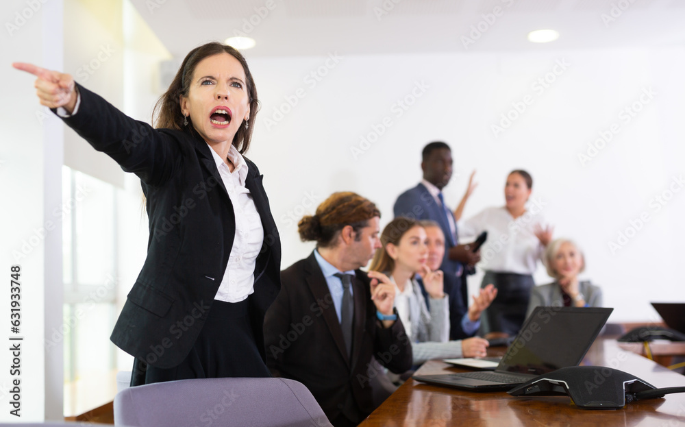 Furious businesswoman screaming at her employees during meeting in conference room.