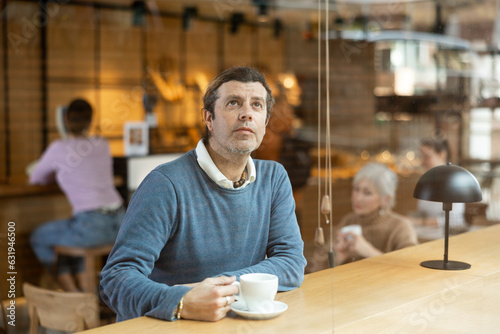 Relaxed man sitting alone drinking coffee in quiet cafe