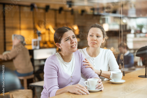 Caring empathetic woman comforting upset younger sister while sitting together at cozy cafe over cup of coffee
