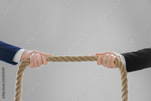 Dispute concept. Men pulling rope on light grey background, closeup